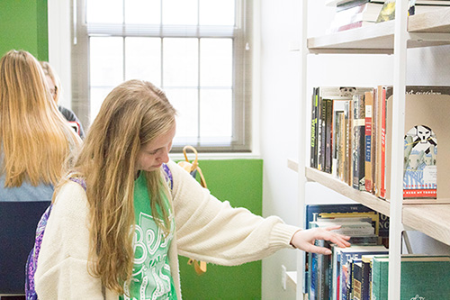 Girl in white sweater and green shirt browsing a bookshelf