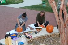 Two female students carving pumpkins by a tree