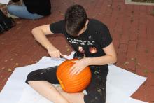 Student carving a pumpkin on the ground