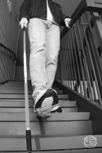 Black and white photo of a person going down the stairs with a cane.