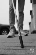 Black and white photo of person feeling the sidewalk with a cane.